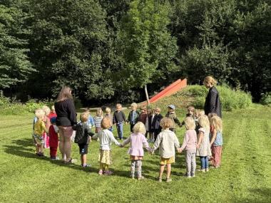 Børn der står i en rundkreds på græsset og holder i hånd